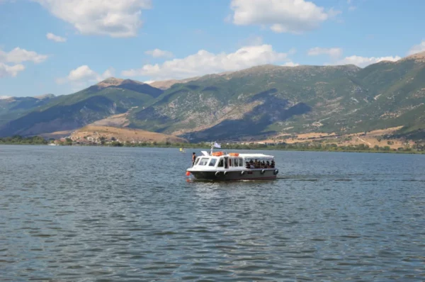 Scenic view of a boat cruising on the calm waters of Ioannina, framed by lush mountains in Greece.