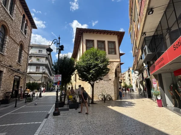 Charming stone buildings and vibrant shops line the streets of Ioannina, Greece, under a bright blue sky.