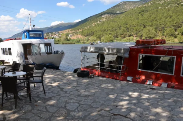 Boats docked by the peaceful waters of Ioannina Island, surrounded by green hills and a clear blue sky.
