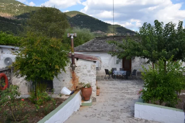 Charming stone house with a courtyard, surrounded by greenery and mountains in Ioannina, Greece, showcasing a peaceful rural setting.