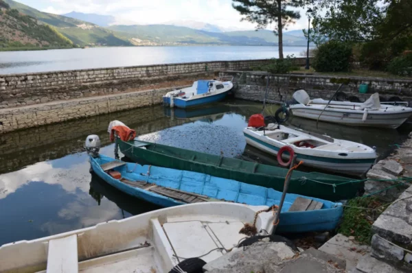 Colorful boats docked at Ioannina Island, Greece, reflecting on calm waters with scenic hills in the background.