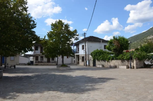 Charming streetscape in Ioannina Island, Greece, featuring rustic buildings, green trees, and a clear blue sky.