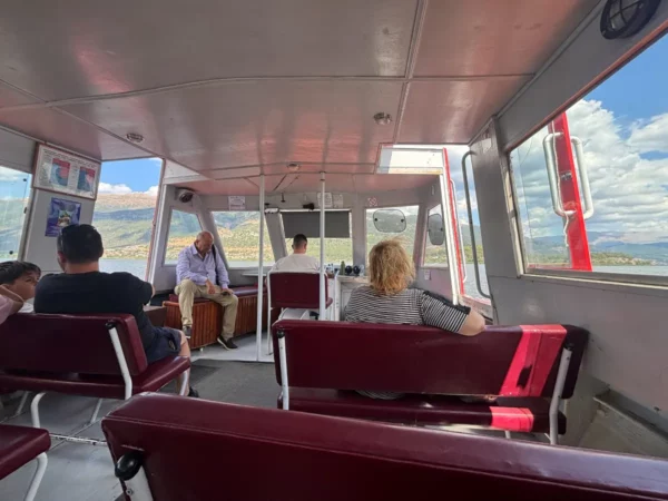 interior of the Ioannina Island ferry with passengers seated and Lake Pamvotida visible through the windows