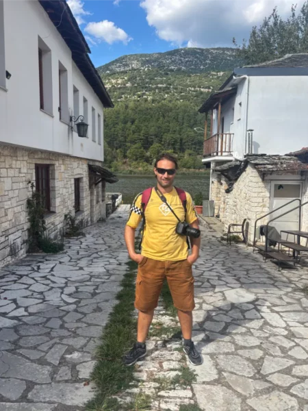 A traveler stands on a stone pathway in Ioannina, Greece, surrounded by traditional stone buildings and lush greenery.