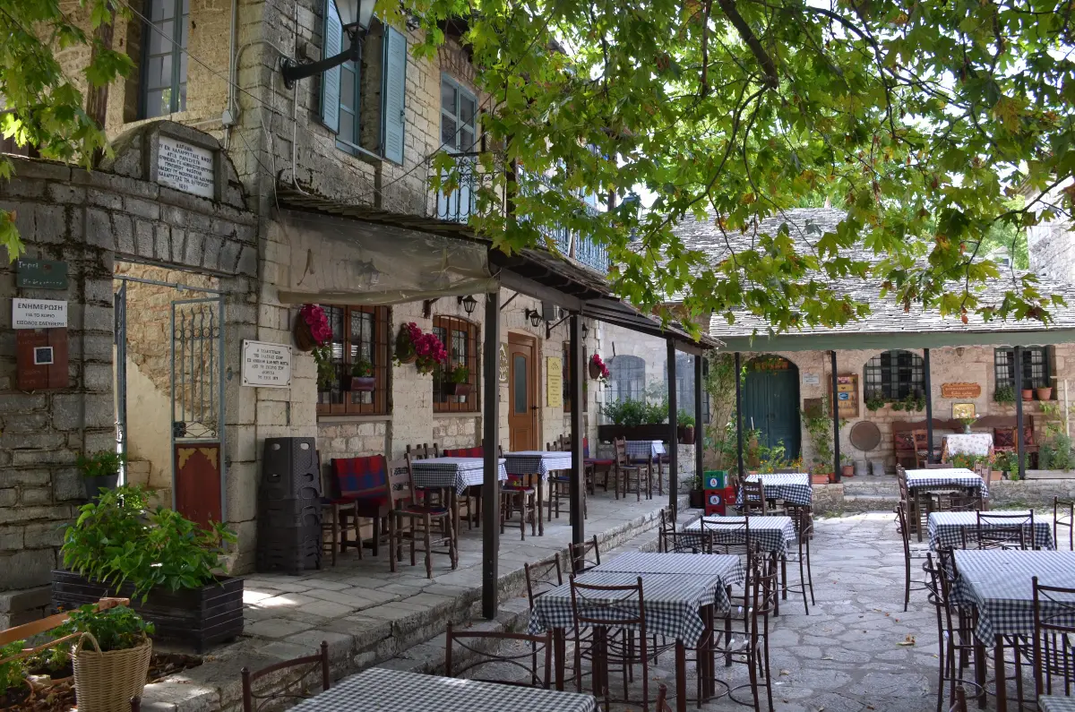 Café terrace in Kalarrytes, Tzoumerka — stone square under plane trees with tables and chairs.