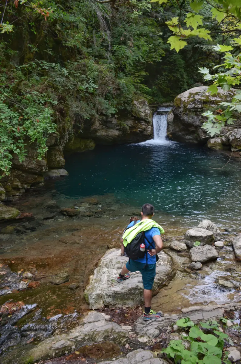 Hiker standing by the turquoise pool at Kouiassa Waterfall in Tzoumerka, Greece.