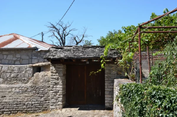 Traditional stone house with a wooden door and a thatched roof, surrounded by greenery in Koukouli, Zagorochoria, Ioannina, Greece.
