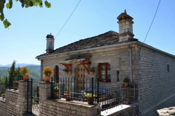Traditional stone house with potted plants, featuring a wooden door and a picturesque balcony in Koukouli, Zagorochoria, Greece.