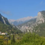 Litochoro town in Pieria, Greece, with the lower slopes of Mount Olympus rising above tiled rooftops and surrounding greenery.