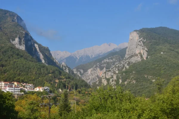 View of Mount Olympus rising above Litochoro, with forested slopes, steep limestone cliffs, and higher peaks visible in the distance.