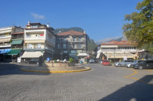 Town square of Litochoro with traditional buildings, parked cars, and Mount Olympus rising in the background.