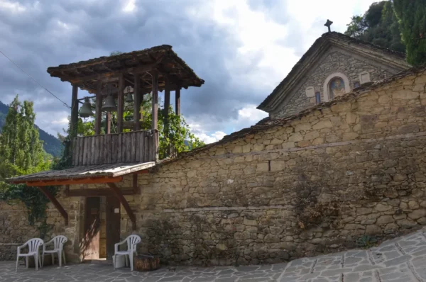 Monastery of Saint Nicholas in Metsovo — stone wall with a wooden bell tower and church roof against the Pindus mountain sky.