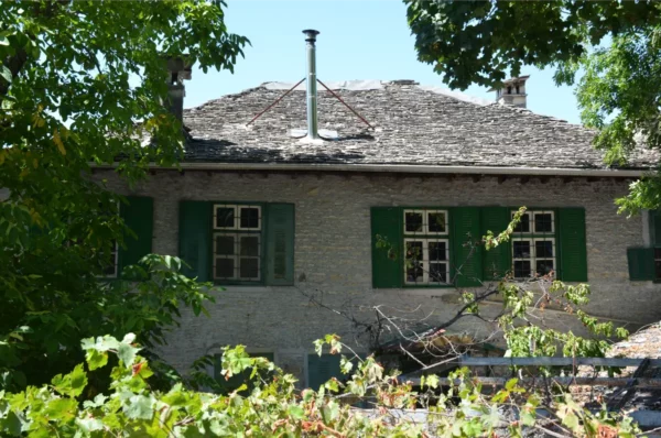 Traditional stone house with green shutters surrounded by lush foliage in Monodendri, Zagorochoria, Ioannina, Greece.