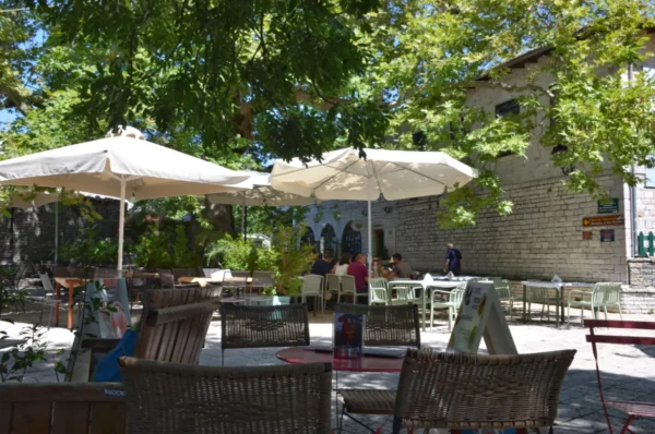 Charming outdoor café in Monodendri, Zagorochoria, Ioannina, Greece, featuring shaded seating and lush greenery.
