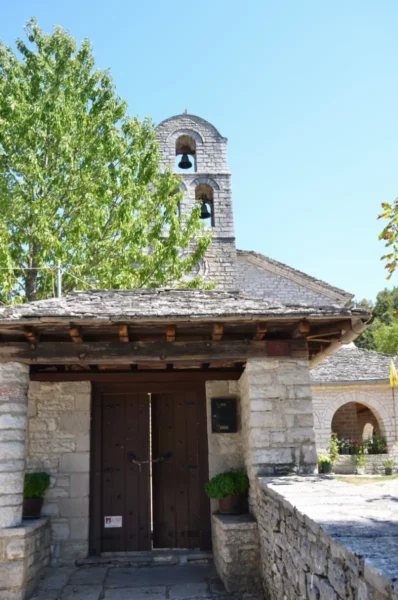 Monodendri features a stone church with a bell tower, surrounded by lush trees and clear blue skies in Zagorochoria, Ioannina, Greece.