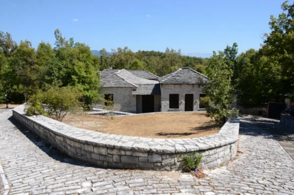 Charming stone house surrounded by lush greenery in Monodendri, Zagorochoria, Ioannina, Greece, under a clear blue sky.