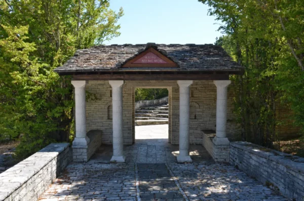Picturesque archway with stone columns leads to a pathway in Monodendri, Zagorochoria, surrounded by lush greenery in Ioannina, Greece.