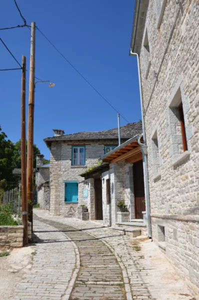 Charming cobblestone path lined with traditional stone houses and vibrant blue windows in Monodendri, Zagorochoria, Greece.