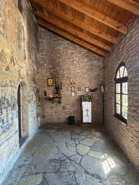 Interior of a stone church in Monodendri, displaying wooden beams, illuminated icons, and a decorative altar in Zagorochoria, Greece.