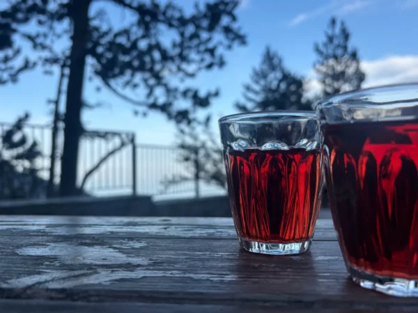 Rich red beverages sit on a wooden table, framed by trees and a scenic view of Mount Olympus in Pieria, Greece.