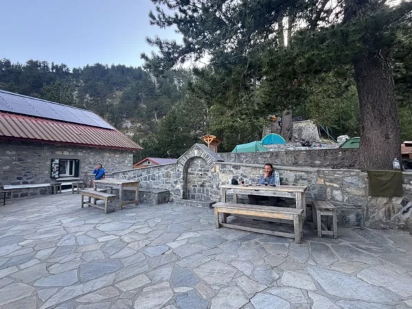 Charming stone patio with wooden tables and two people enjoying the serene surroundings at Mount Olympus, Pieria, Greece.