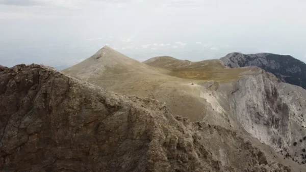 Mount Olympus rises majestically in Pieria, Greece, showcasing rugged peaks and a dramatic landscape under a cloudy sky.