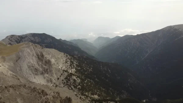 Breathtaking view of rugged mountains and misty valleys surrounding Mount Olympus in Pieria, Greece, under a cloudy sky.