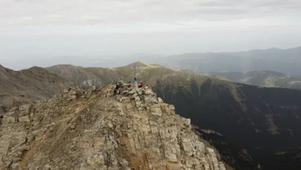 Breathtaking view from Mount Olympus, showcasing rocky peaks and vast green valleys of Pieria, Greece, under a cloudy sky.