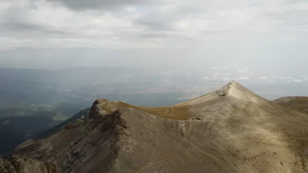 Dramatic peaks of Mount Olympus rise under a moody sky, showcasing rocky terrain and distant valleys in Pieria, Greece.