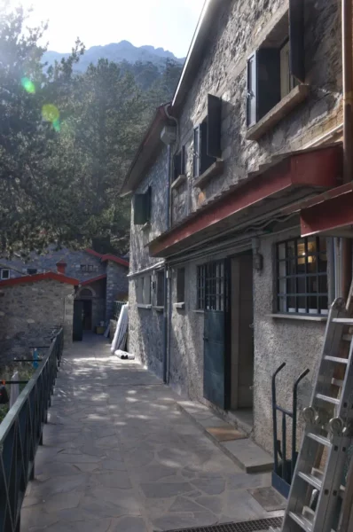 Charming stone buildings line the pathway at Mount Olympus, surrounded by lush greenery in Pieria, Greece.