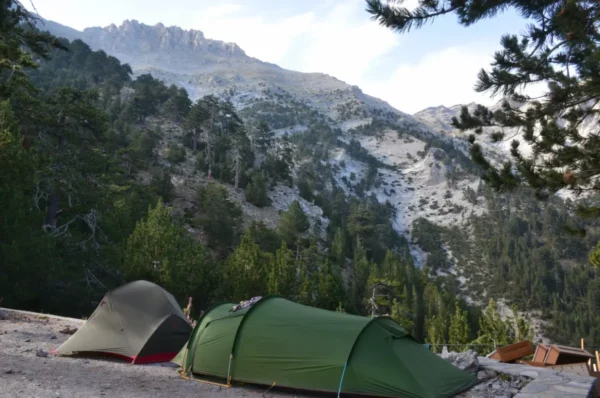Camping tents sit amidst lush greenery with Mount Olympus rising majestically in the background, highlighting the natural beauty of Pieria, Greece.
