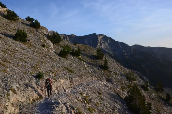 Hiker traverses a rocky path on Mount Olympus, surrounded by rugged terrain and scenic views in Pieria, Greece.
