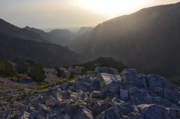 Golden sunlight illuminates rocky terrain and distant mountains at Mount Olympus, Pieria, Greece, creating a serene landscape.