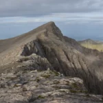 Rocky ridge on Mount Olympus near Mytikas peak, with steep limestone slopes and distant views toward the Aegean Sea.