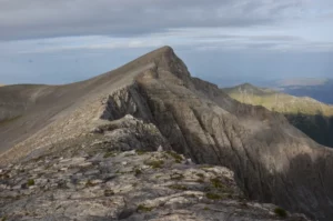 Rocky ridge on Mount Olympus near Mytikas peak, with steep limestone slopes and distant views toward the Aegean Sea.