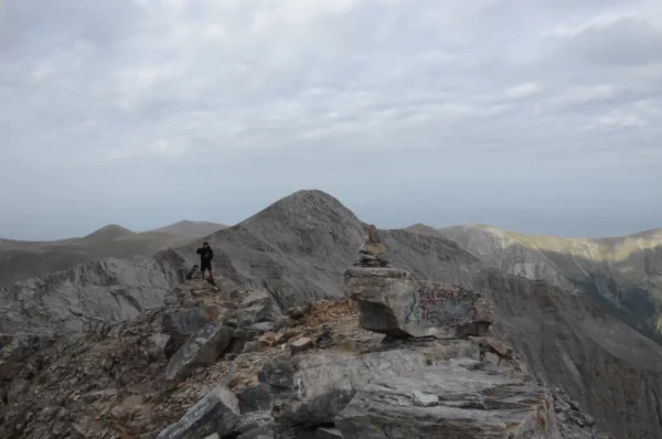 Rugged mountain terrain at Mount Olympus in Pieria, Greece, with a hiker navigating the rocky summit under a cloudy sky.