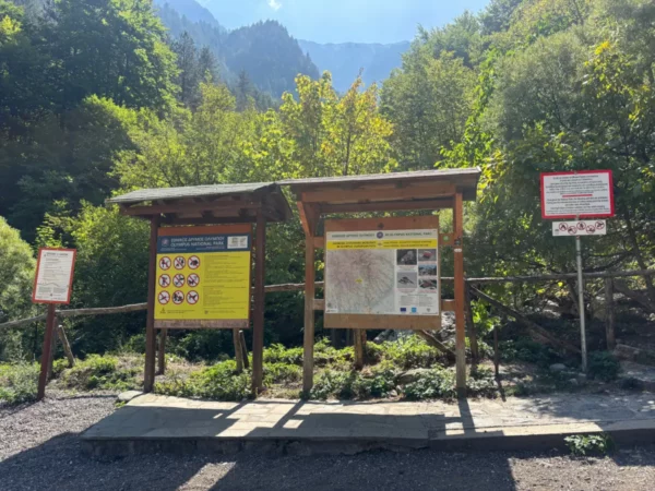 Informative signs guide visitors at Mount Olympus in Pieria, Greece, surrounded by lush greenery and distant mountains.