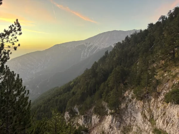 Dramatic sunset over Mount Olympus in Pieria, Greece, highlighting the rugged terrain and lush green forested slopes.