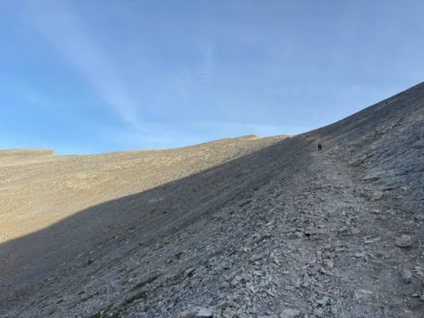 Rocky terrain leading up Mount Olympus in Pieria, Greece, under a clear blue sky and soft shadows cast by the incline.