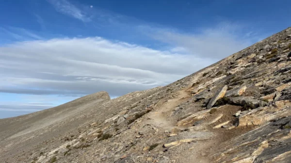 Rocky trails and rugged terrain lead up the slopes of Mount Olympus in Pieria, Greece, under a bright blue sky.