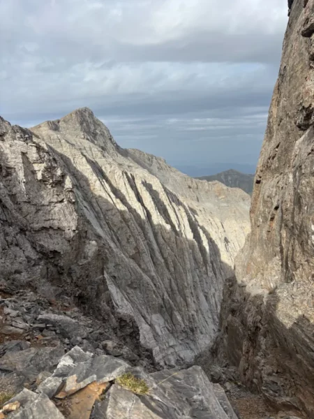Majestic rocky cliffs and steep ravines of Mount Olympus, showcasing dramatic shadows and a cloudy sky in Pieria, Greece.