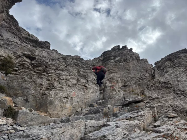 Climber ascending rugged rocky terrain under a cloudy sky on Mount Olympus, Pieria, Greece.
