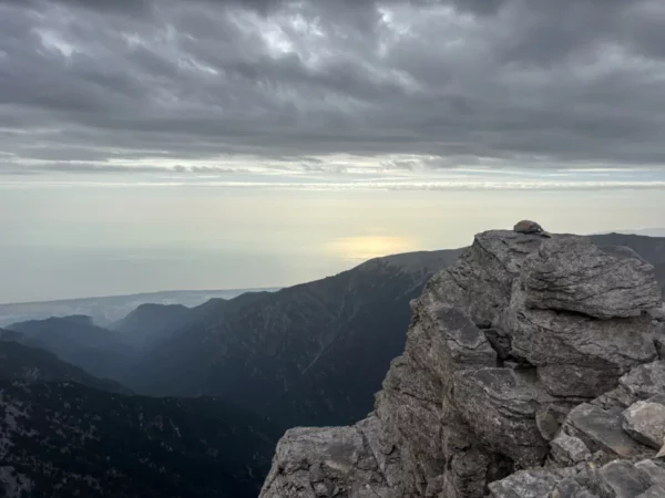 Dramatic rocky summit of Mount Olympus with overcast skies and a distant view of the sea in Pieria, Greece.
