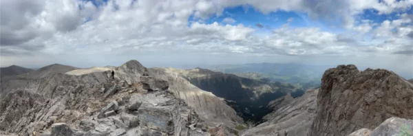 Stunning panoramic view from Mount Olympus, featuring rocky peaks and a vast landscape under a cloudy sky in Pieria, Greece.