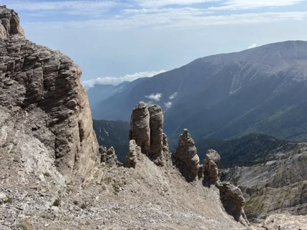 Dramatic rock formations rise above the landscape of Mount Olympus, with distant mountains and a stunning sky in Pieria, Greece.