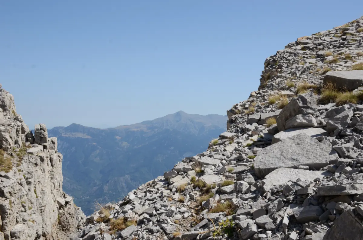Rocky mountain ridge on Mount Tymfi overlooking deep valleys of the Pindus Mountains, with distant peaks fading into the hazy summer horizon.