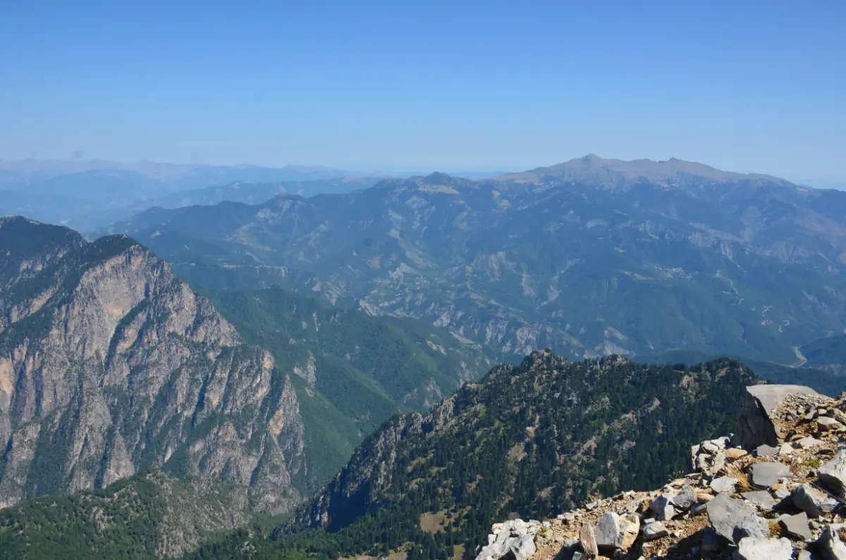 View of Mount Smolikas and Mount Grammos from Gamila Peak on Mount Tymfi, with layered ridges of the Pindus Mountains under clear summer skies.
