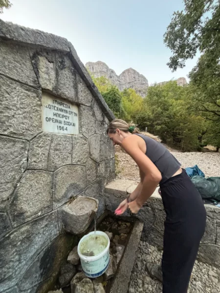 Woman washing at a stone mountain spring on the Mount Tymfi trail, a traditional hiking water source in the Zagori region of northern Greece.