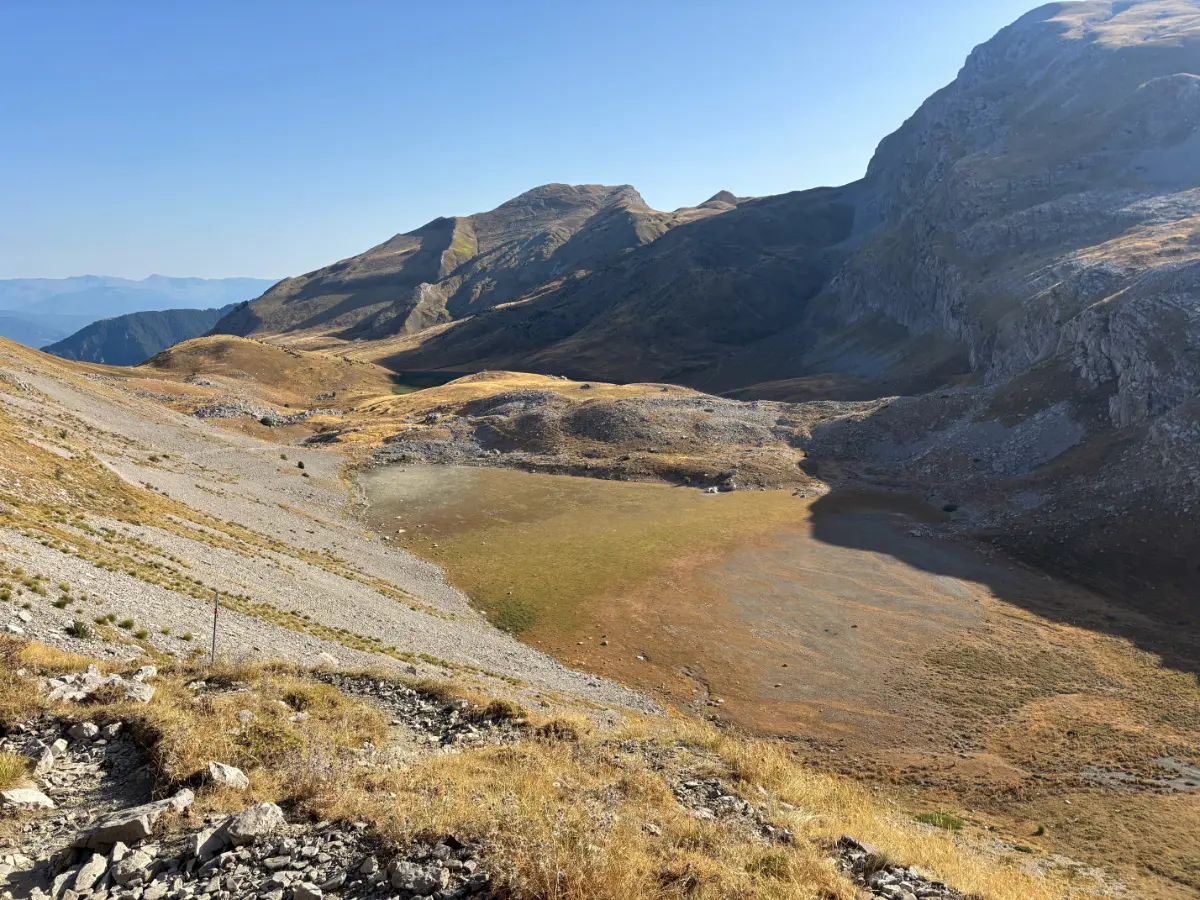 Wide karst basin of Mount Tymfi with the seasonal alpine lake of Xeroloutsa Tsoumani, surrounded by barren limestone slopes under clear summer light.