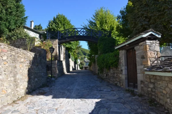 Stone bridge linking the twin Sossidis mansions in Nymfaio village, Florina, spanning a cobbled lane between traditional stone buildings.